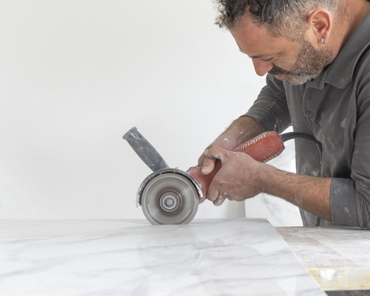 Craftman in grey shirt cuts a gray marble tile using an angle grinder. Man at work, hands closeup. House construction or DIY rennovation. Expert tile cutting techniques
