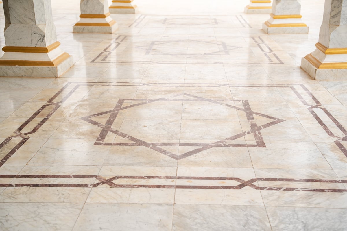 Mosque marble floor with geometric inlay pattern featuring eight pointed star motif between column bases in open courtyard. Islamic architecture, decorative flooring, exterior detail.