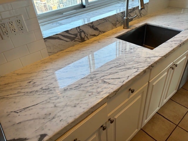 Modern kitchen with marble countertop, white cabinets, black sink, and window view overlooking city buildings — after professional restoration